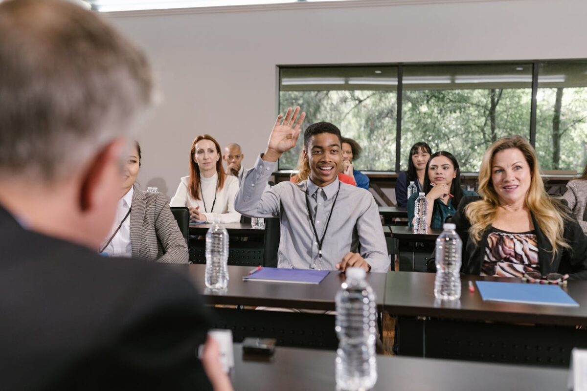Businesspeople in a conference room engaging in a discussion, with a man raising his hand.