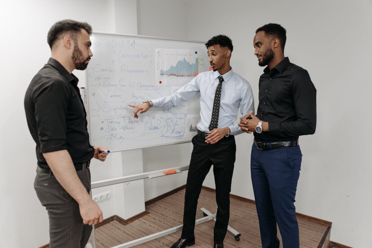 Three professionals discussing strategies at a whiteboard in an office setting.